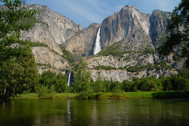 Lush flora frame this view of Yosemite Falls in late spring with the river water in the foreground, Yosemite National Park, CA