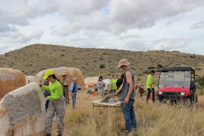 Youth Summit participants complete preservation work on the Post Trader's Store. Two students from the Arizona Youth Summit add mud to the wall of the Post Trader's Store as a part of their field school experience. Other youth summit participants and instructors can be seen in the background.