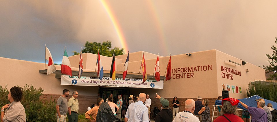 a group of people stands outside a building reading "Information Center." A rainbow is overhead.