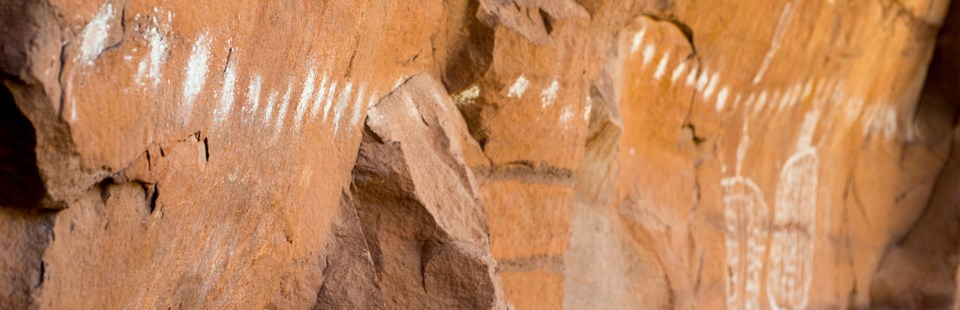 a rock wall with a long row of white dots painted on it. some round white figures are painted in the background