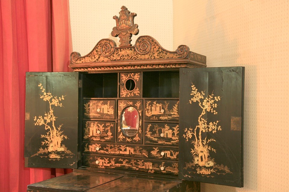 Black lacquer and gilt sewing cabinet with front cabinet doors open revealing a small oval mirror and drawers.