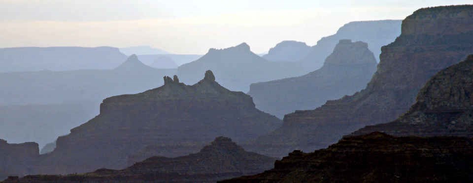 Silhouettes of Grand Canyon rock formations as afternoon light filters through them.