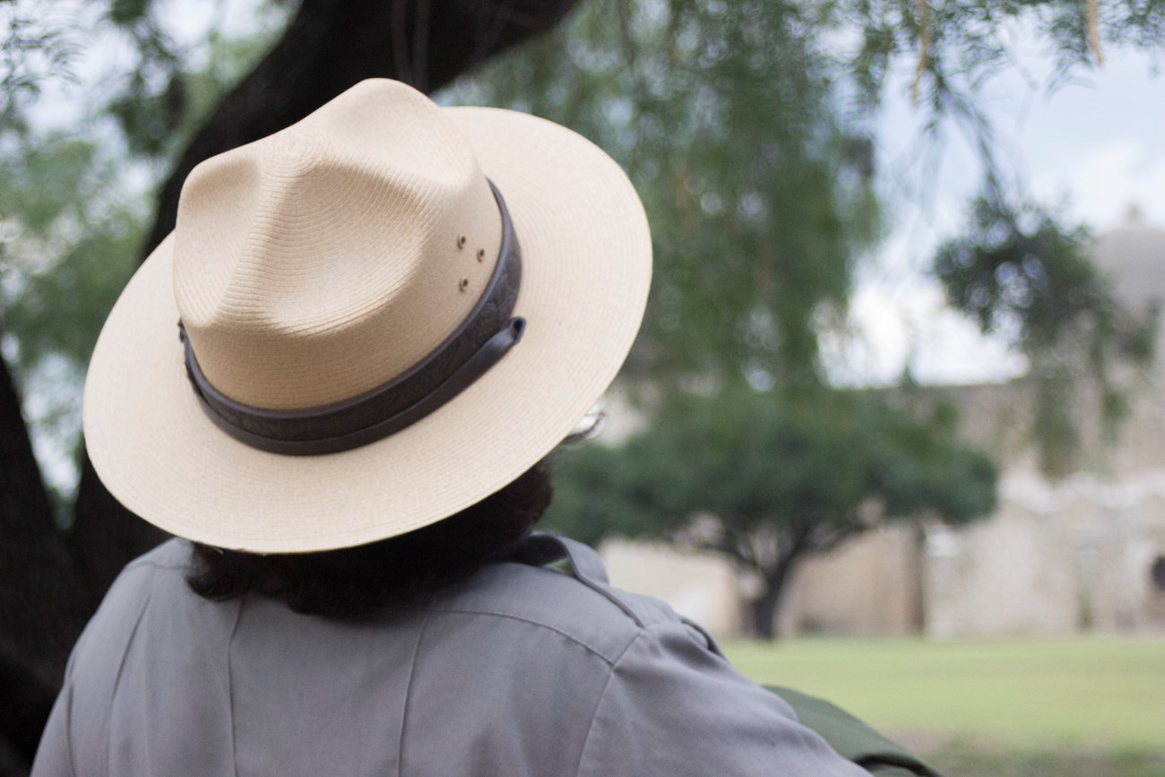 Ranger wearing hat looks to Spanish mission