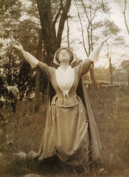 Woman in colonial clothes, kneeling, with arms outstretched, pointing upward
