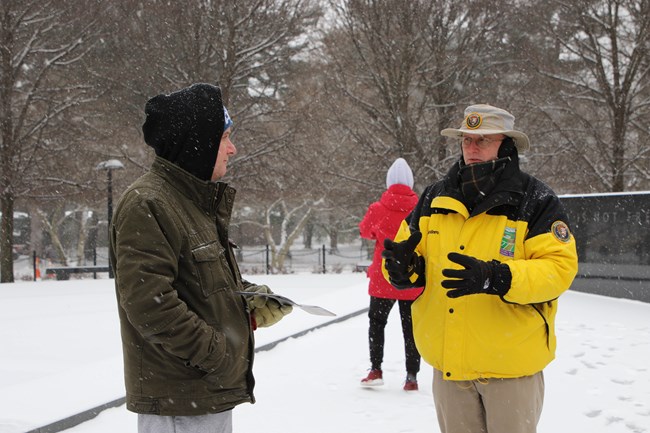 Volunteer talking to a visitor at the Korean War Veterans Memorial after a snowfall