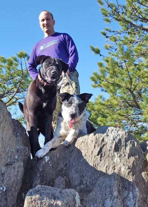 Two dogs and a man looking down from a boulder outcrop