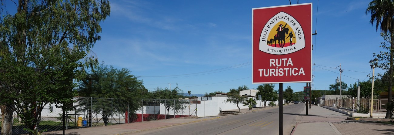 A sign in Spanish along a street marking the Anza trail