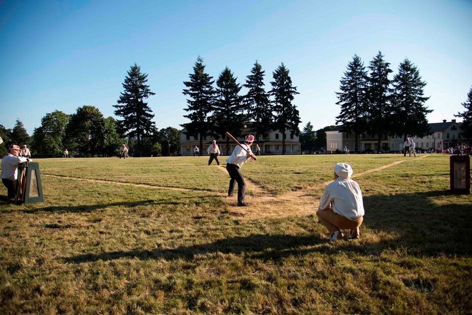 Photograph taken from behind home plate as costumed base ball players play at Vancouver Barracks