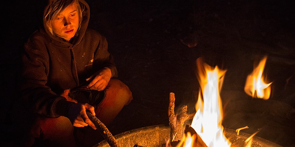 A youth sits next to a campfire