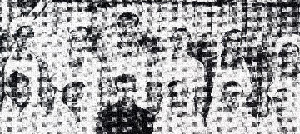 Black and white photo of young men wearing cook's aprons and hats.