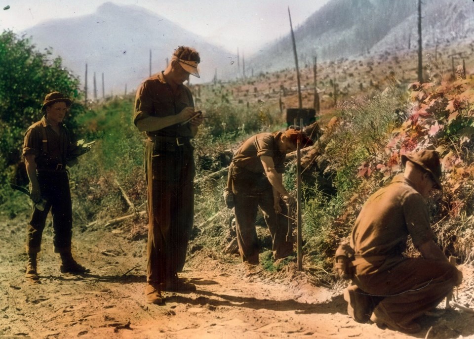 Colorized black and white photo of men in work clothes in forested area.