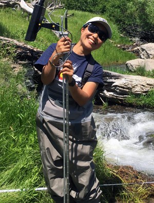 Intern holding equipment next to mountain stream Intern holding equipment next to mountain stream