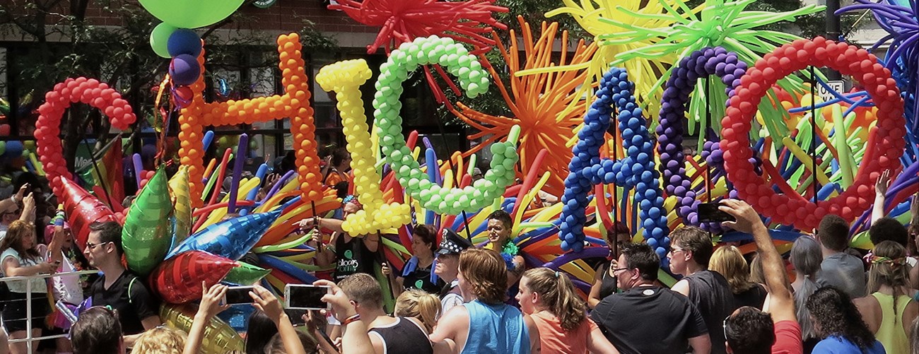 People in a crowd holding rainbow colored balloons that spell CHICAGO