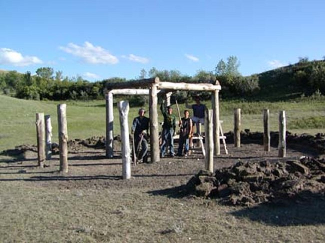 4 men stand under scaffolding of earth lodge.