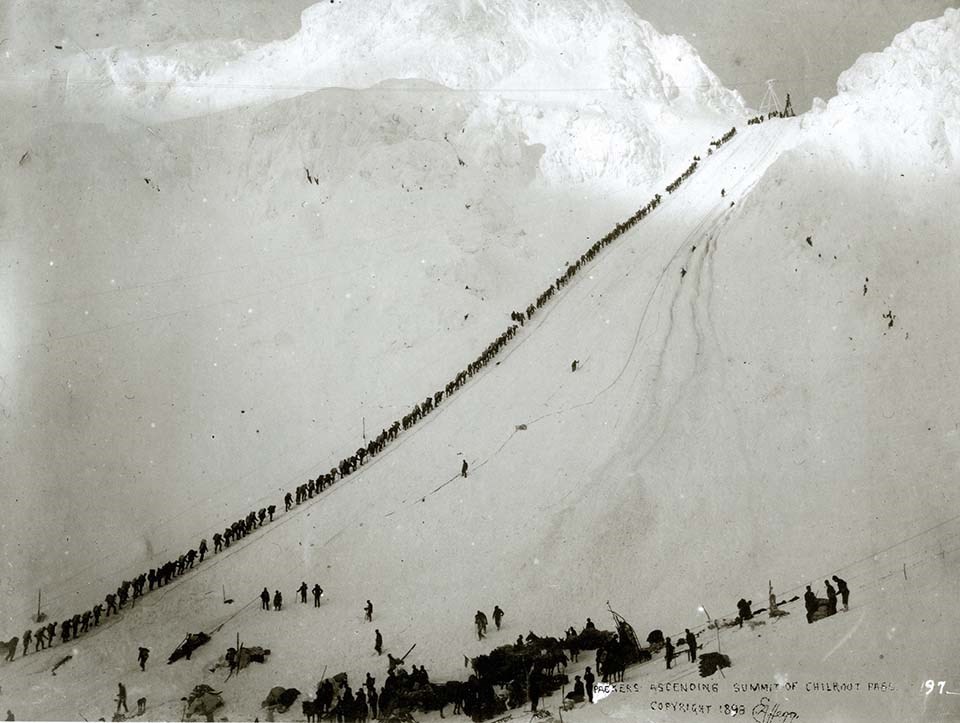 A historical photo of a line of stampeders climbing the Chilkoot trail in the winter.