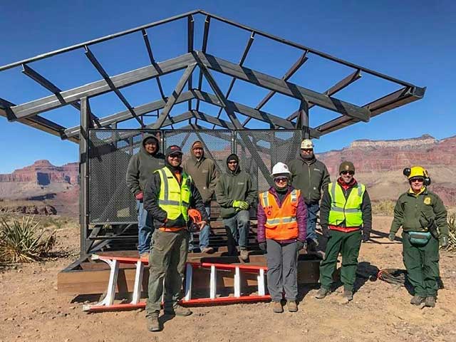 8 workers wearing safety vests and helmets are standing in front of the framework of a partially assembled shade structure 12 x 24 feet.