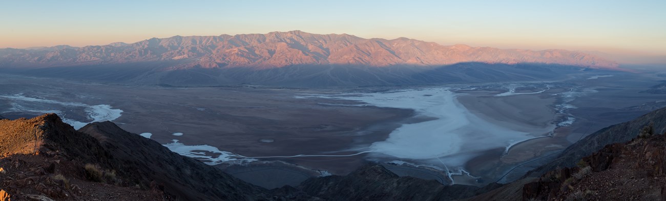 A panoramic image of the sun rising on a desert mountain range.