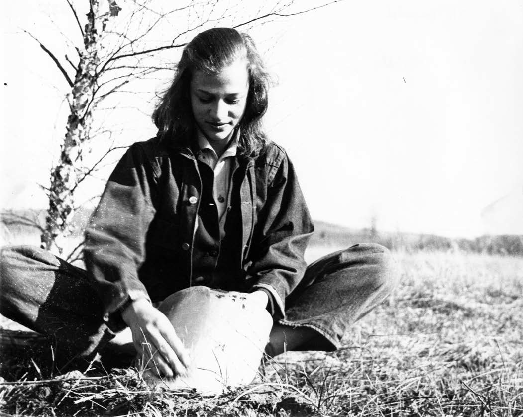 A young woman sits on the ground cleaning a shovel.