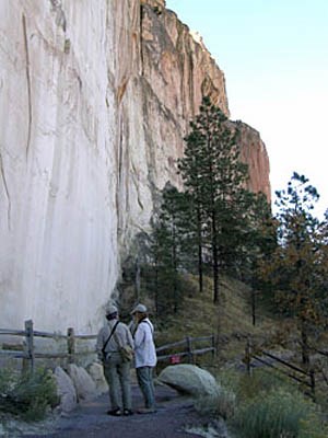 Two people stand at base of large stone wall.