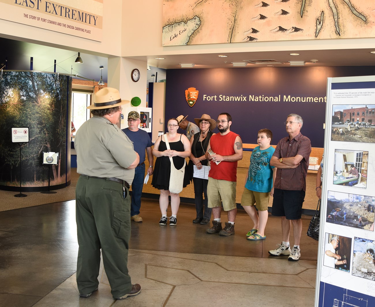 Ranger Dael Leading Tour a park ranger stands in front of a colorful crowd at a visitor center, and points at a map.