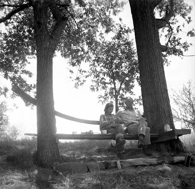 Estella & Aldo Leopold A young woman sits with an older man on a bench under a tree.