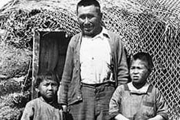 An Alutiiq man and two children stand together in this historic photo.