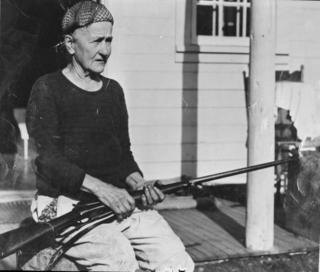 fannie 1 a woman sitting on a porch holding a rifle