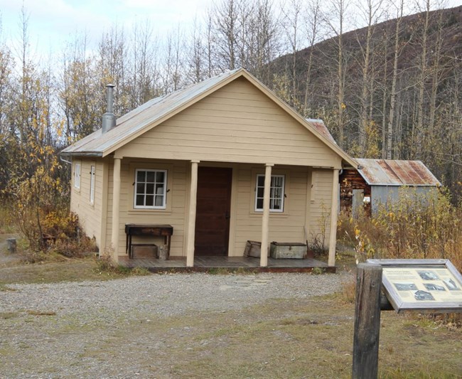 a one-story clapboard house sitting in a forest