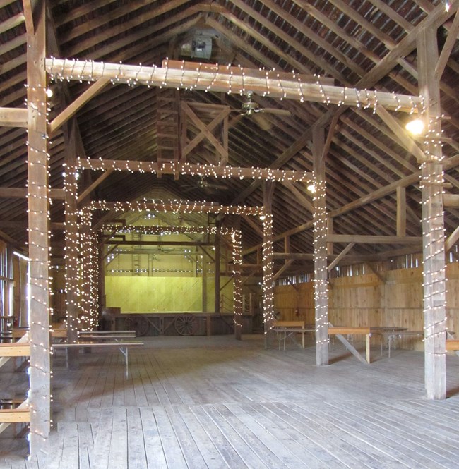 Festhalle Barn gathering space Open wooden rafters, walls, and floors decorated with small, white lights.