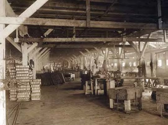 Black and white photo of interior of a large building with lots of cans and work benches.