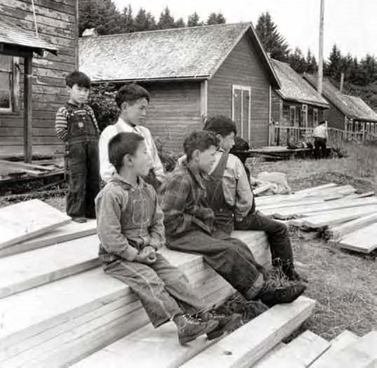 Black and white photo of six boys sitting on piles of lumber.