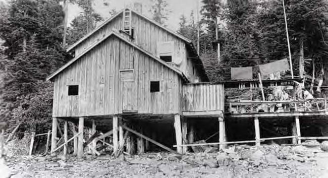 Black and white photo looking at a large wooden building on piers