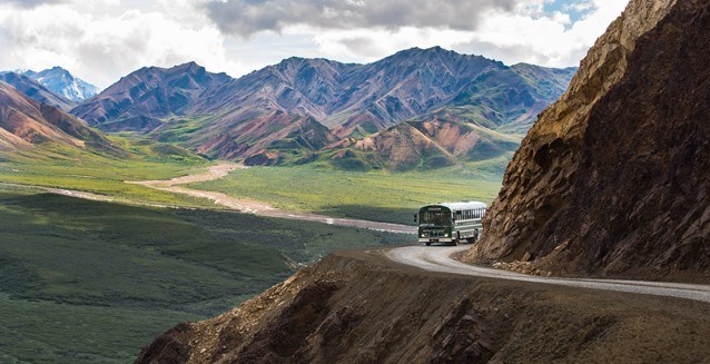 a bus driving on a dirt road perched on the side of a mountain