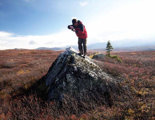 a man standing atop a boulder, taking a photo of it
