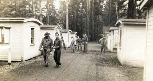 Black and white photo of men standing between rows of identical small houses.