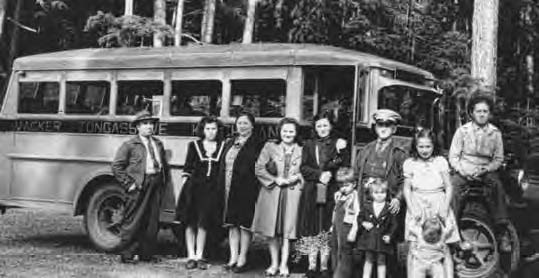 Black and white photo of 11 people from baby to adult standing in front of a bus.