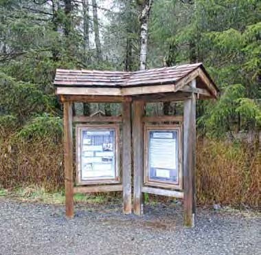 Information kiosk on gravel surface in front of trees.