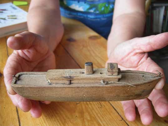 A set of hands holding a yellowed, wooden toy boat.