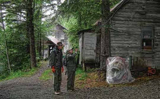 Modern photo of two people in rain gear standing on a path near trees and old wooden buildings