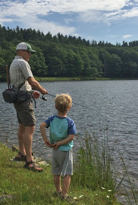 A man and young boy fishing on the grassy bank of a lake