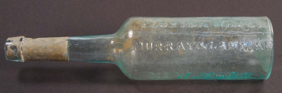 Colorless glass bottle with long neck and raised lettering