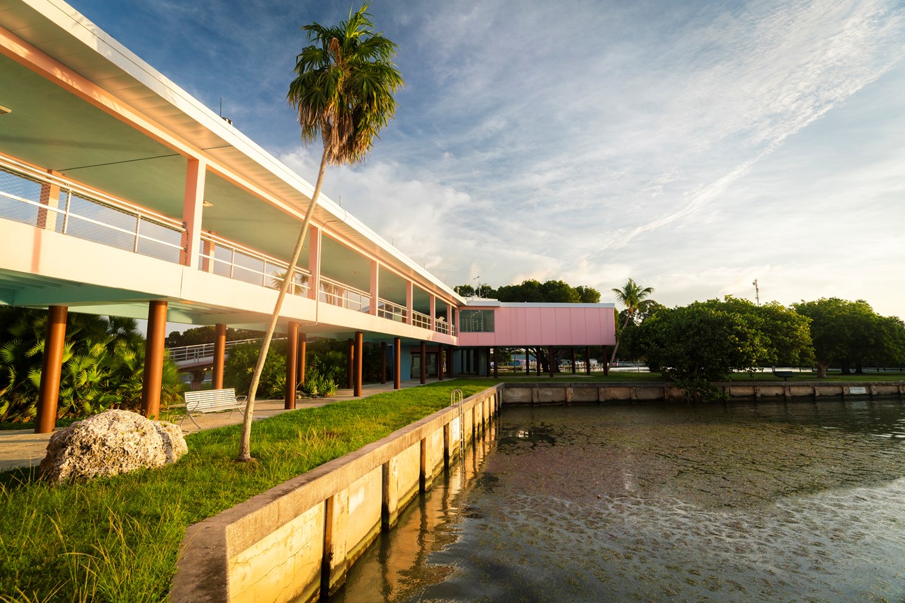 A two-story pink building above a seawall along the ocean.