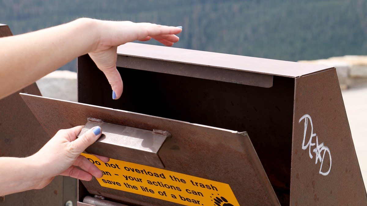 hands open trash can designed to keep bears out