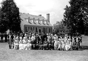 Rows of people in colonial costumes pose in front of 'replica' birthplace mansion.