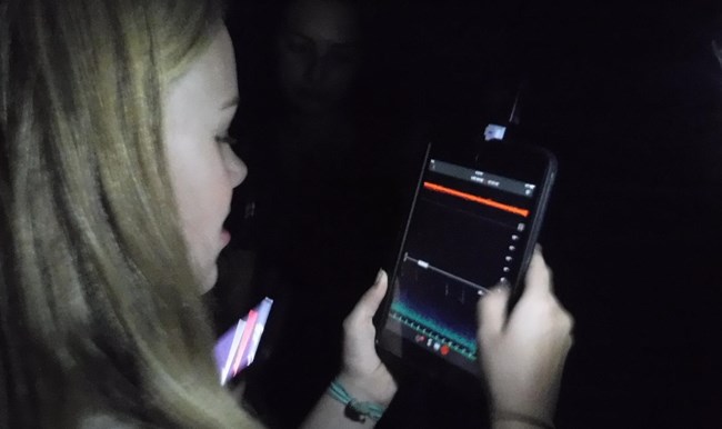 A young girl holds a device to monitor bats in the area by locating their calls