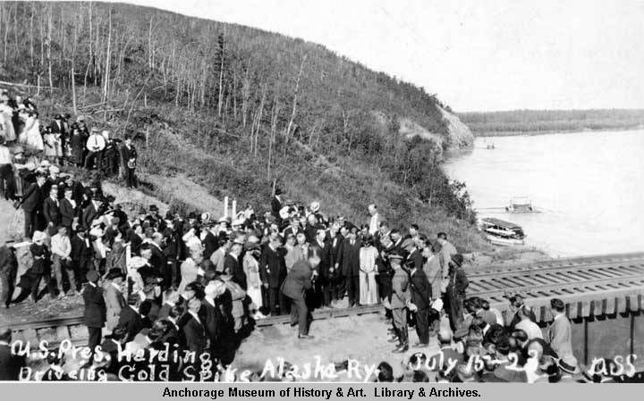 crowd of people watching a spike being driven into a railroad bridge over a river