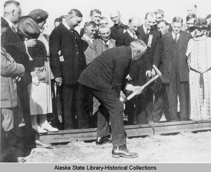 a man hammering a spike into a railroad while surrounded by a crowd