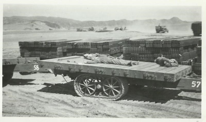 Black and white photo of men laying of a flatbed vehicle with equipment stacked behind them