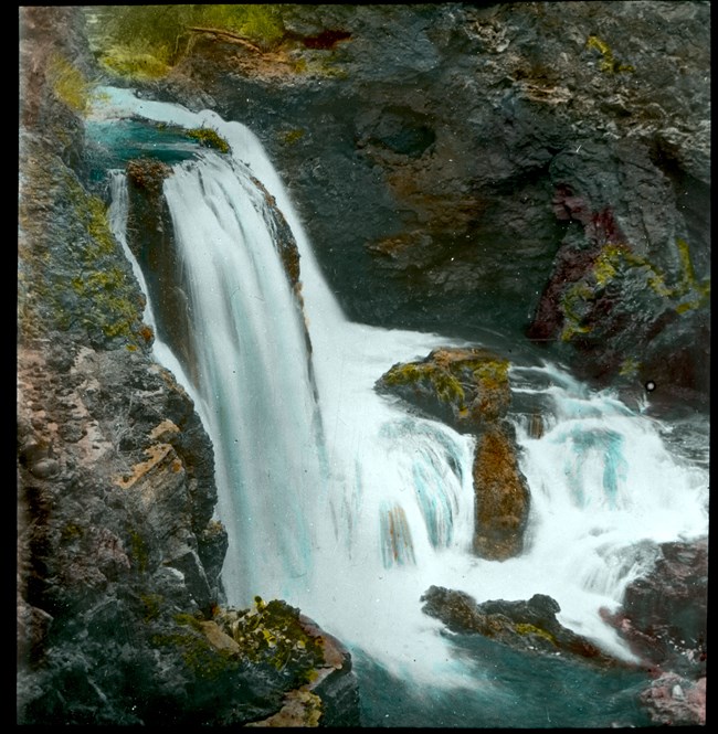 Beaver Canyon Waterfall A waterfall pours over dark rocks into a clear blue pool.