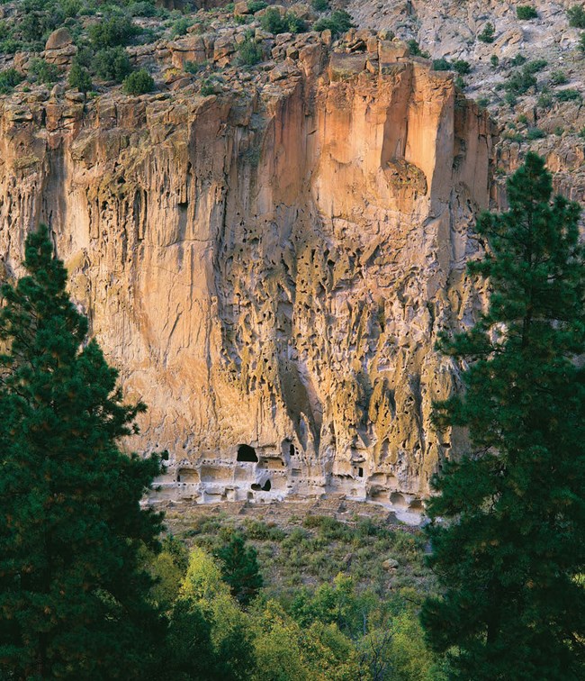 ruins carved into the rock with cliff towering above